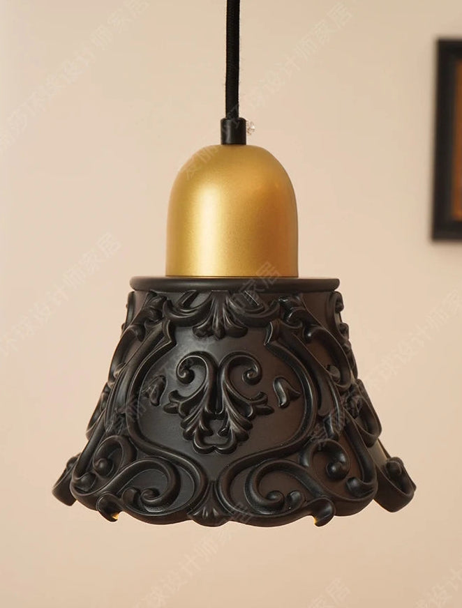 Decorative pendant light with gold bulb and black intricate base on beige background