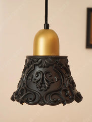 Decorative pendant light with gold bulb and black intricate base on beige background
