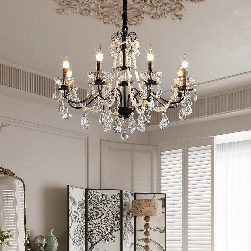 A black candelabra chandelier with crystal and pearl accents is shown in a well-lit room with decorative folding screens and blinds.