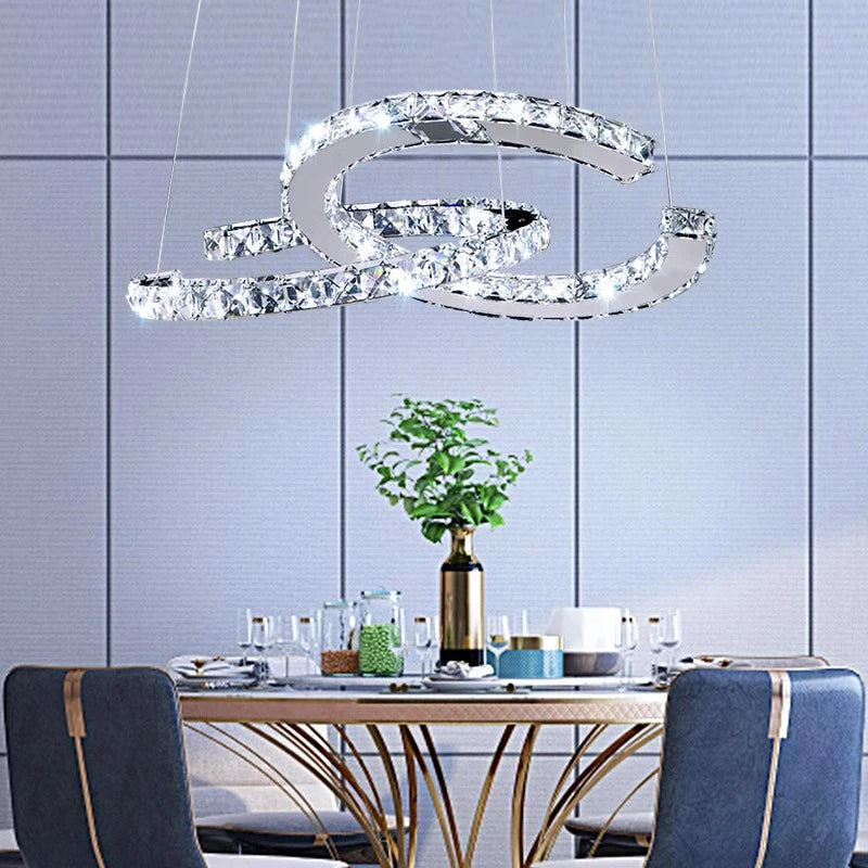 Modern chandelier hanging above a dining table with chairs in a room with tiled walls.