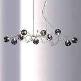 Chrome spiral wave pendant light with multiple smoky gray glass globes suspended against a white background.