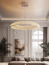 A circular gold chandelier made of small square crystals hanging in a room with white walls and large windows.