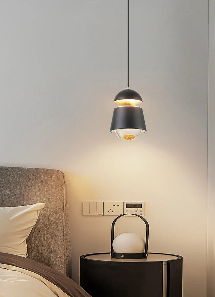 Modern pendant light hanging above a bedside table with a lamp in a bedroom setting.