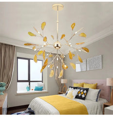 Gold leaf-shaped chandelier with yellow accents hanging in a bedroom with grey walls and yellow bedding.