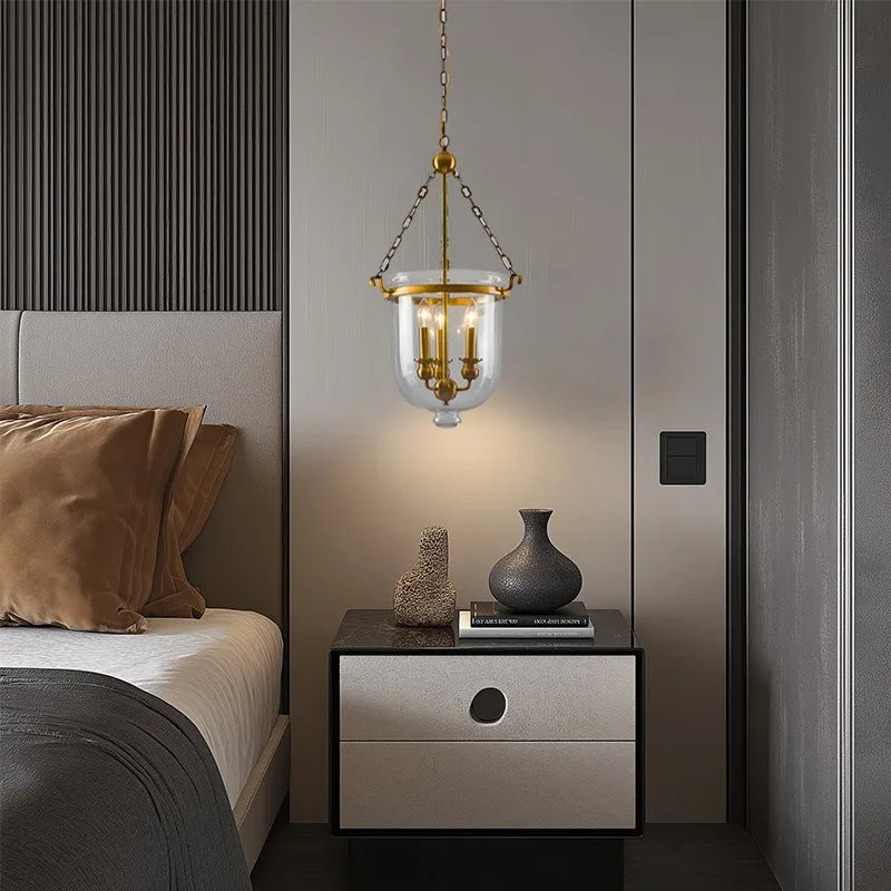 Polished copper and clear glass drum pendant light above a nightstand in a bedroom