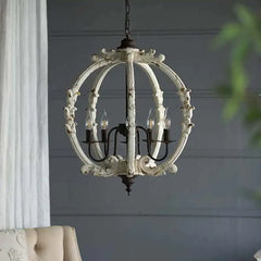 A distressed white carved wood globe chandelier with ornate detailing, suspended from a chain against a dark wall.