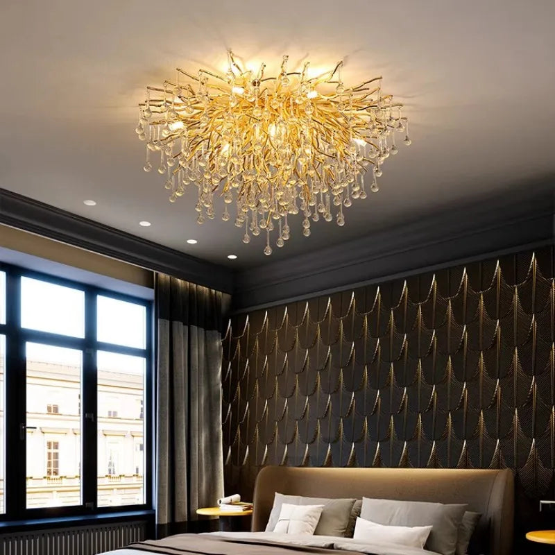 A round, gold crystal chandelier with a branch-like design and teardrop crystals hanging above a bed.