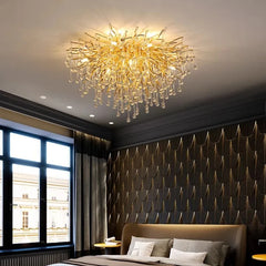 A round, gold crystal chandelier with a branch-like design and teardrop crystals hanging above a bed.