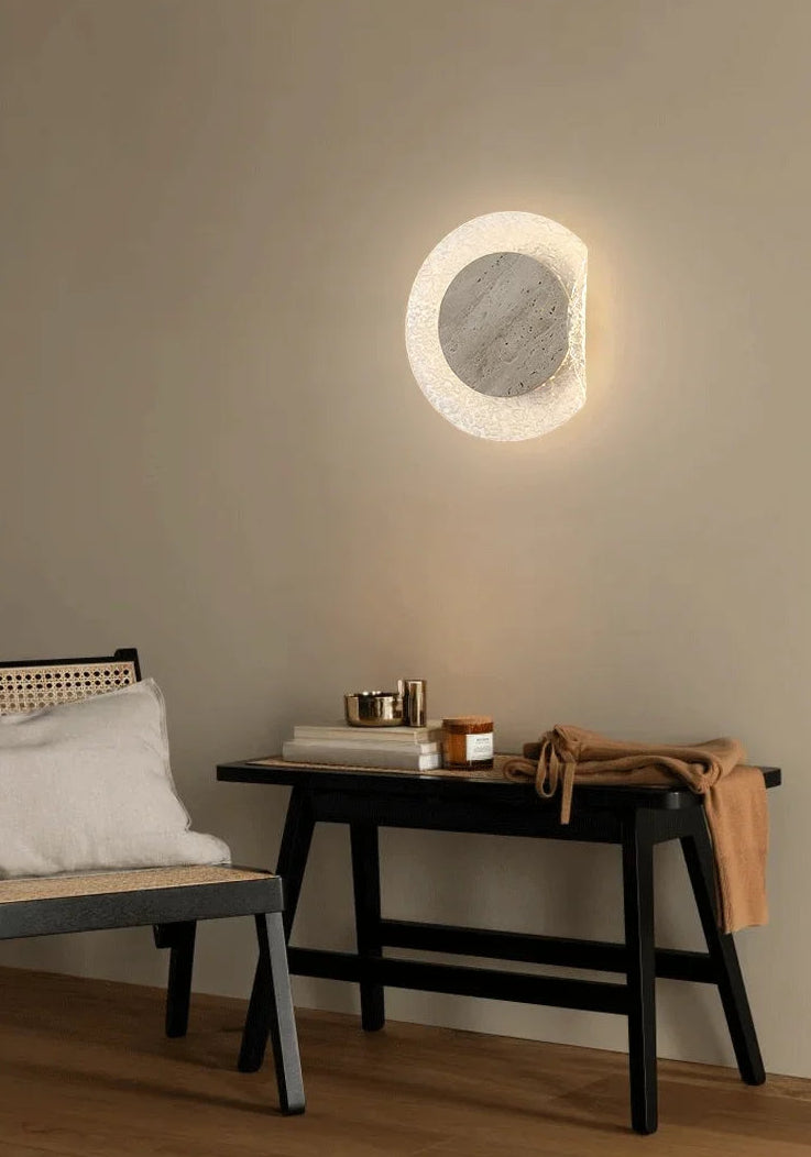 Round wall light fixture on a beige wall with a bench and table in the foreground.