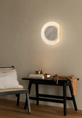 Round wall light fixture on a beige wall with a bench and table in the foreground.