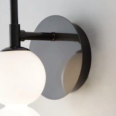 Modern wall-mounted light fixture with black metal arm and glass shade on a neutral background
