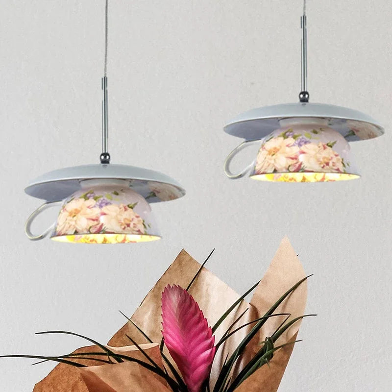 Two floral ceramic pendant lights hanging against a white wall, with a pink bromeliad flower in the foreground.