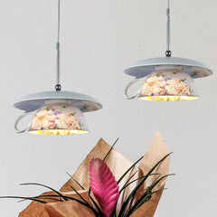 Two floral ceramic pendant lights hanging against a white wall, with a pink bromeliad flower in the foreground.