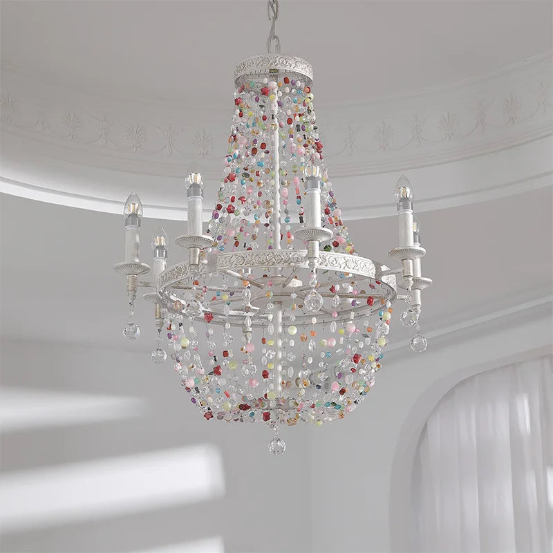 A whimsical chandelier with white metal arms and strings of colorful beads and crystals, casting light.