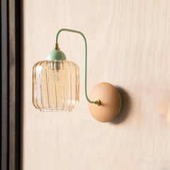 Wall-mounted light fixture with glass shade and wooden base on a neutral wall.