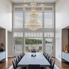 Modern dining room with a large chandelier, table, and chairs in a home with high ceilings and large windows.