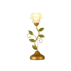 A white background product shot of a gold table lamp shaped like a flower with a glass shade and green leaves.