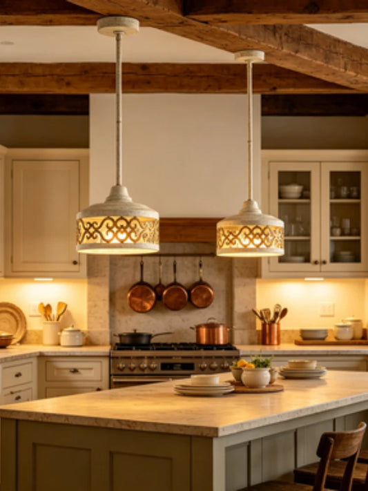 Overhead view of a kitchen island with two white drum pendant lights, each featuring gold scrollwork, hanging above the countertop.
