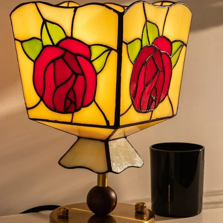 Stained glass lamp with rose design next to a black candle holder on a neutral background