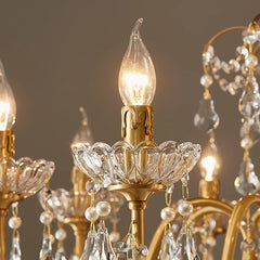 A close-up of a single candle-style light bulb on the gold chandelier, set within a decorative crystal holder.