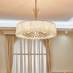 Gold crystal waterfall chandelier suspended in a room with sheer curtains in the background.