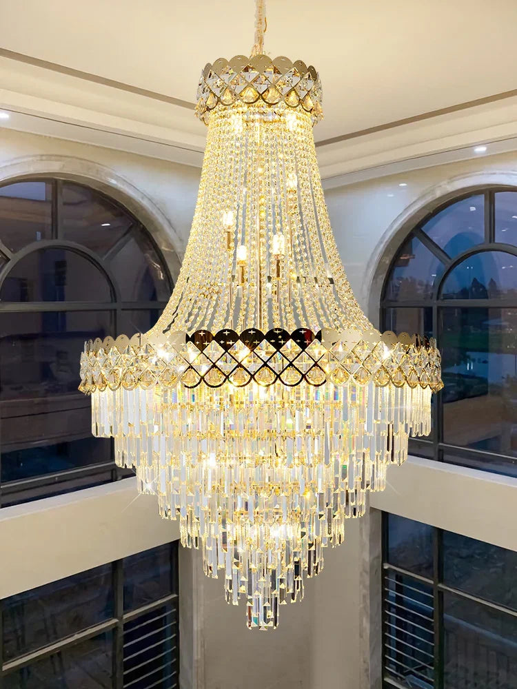 A large gold chandelier with cascading crystal accents, installed in a high-ceilinged room with arched windows.