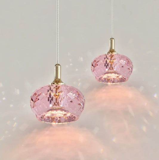 Two pink faceted crystal pendant lights with gold accents hanging against a white background, casting light patterns.