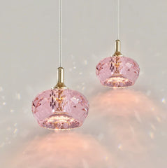Two pink faceted crystal pendant lights with gold accents hanging against a white background, casting light patterns.