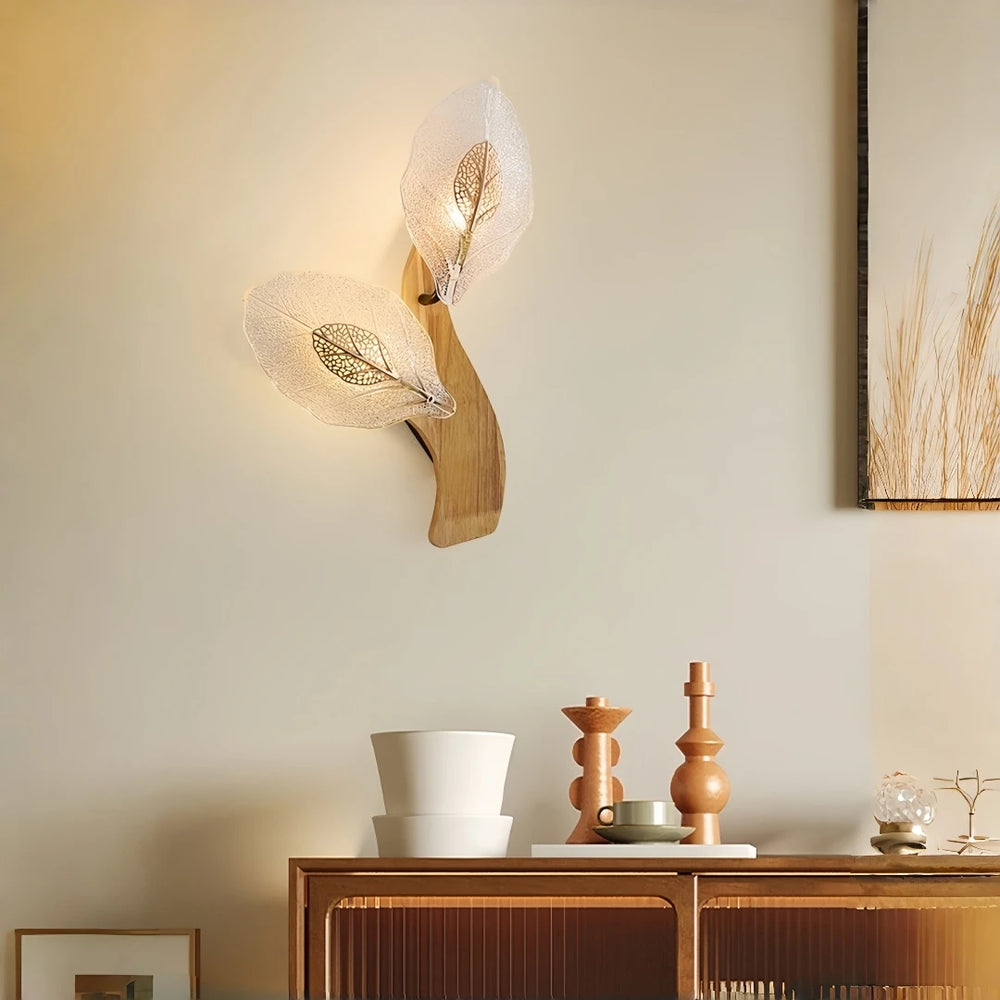 Wood leaf wall sconce with two frosted glass shades, mounted on a light wood base above a wooden cabinet with decorative items.