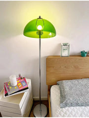 A green mushroom-shaped floor lamp casting a warm glow next to a bed with a wooden headboard.