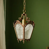 A polished copper pendant light with ornate detailing and frosted glass panels, hanging against a green background.