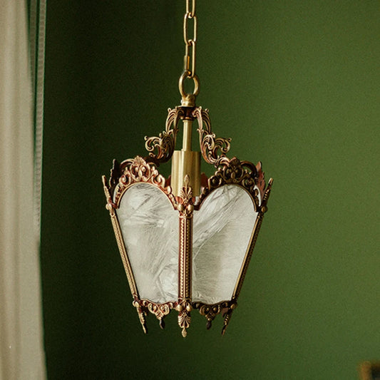 A polished copper pendant light with ornate detailing and frosted glass panels, hanging against a green background.