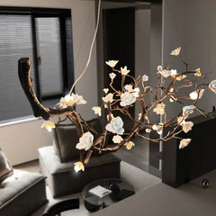 An angled shot of a unique copper chandelier with a natural branch and flower motif, emitting a warm glow in a softly lit interior space.