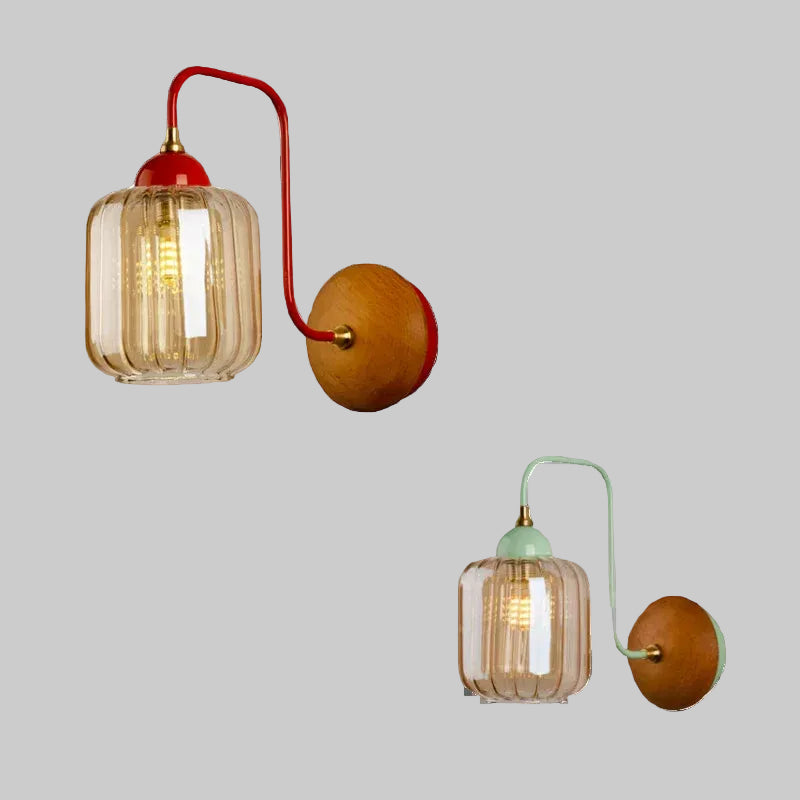 A composite image showing two wall sconces against a grey background: one with a red arm and one with a green arm, both featuring amber glass shades and wooden backplates.