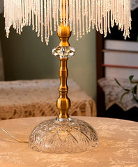 Decorative lamp with crystal base and gold accents on a table with floral arrangements.