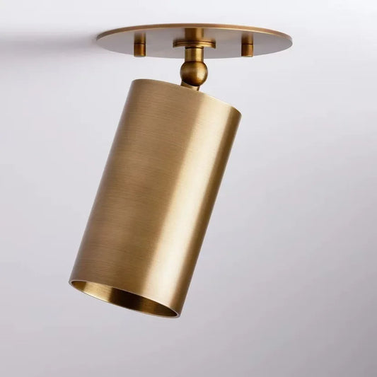 Close-up of a single brushed brass cylinder spotlight mounted on a white ceiling, angled downwards.