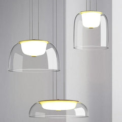 Three clear glass dome pendant lights with gold accents hanging against a light gray background.