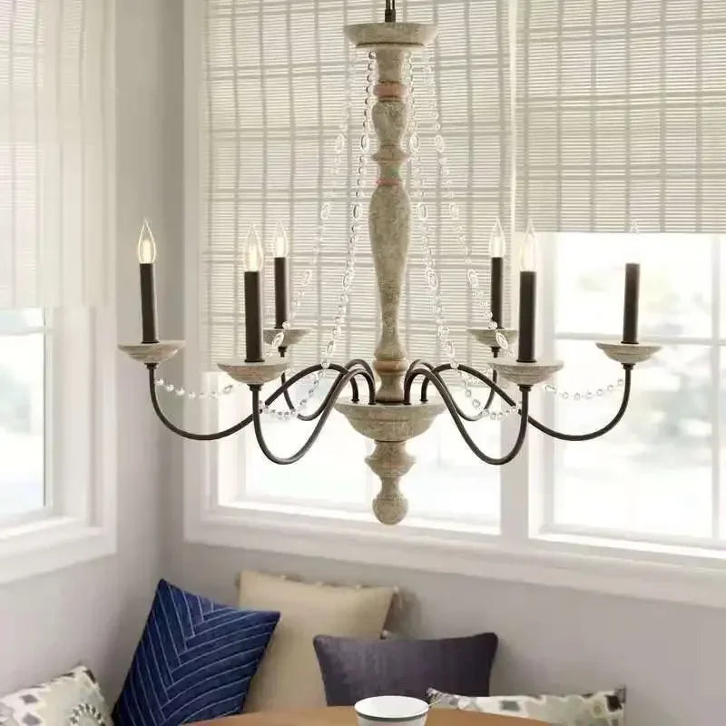 A distressed wood candelabra chandelier with crystal accents hanging above a dining table in a room with bamboo blinds.