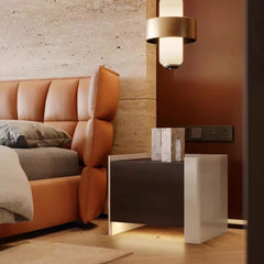 A bedside table next to a bed with an orange headboard, showing a wall-mounted light fixture.