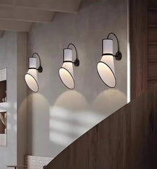 Three wall-mounted lights on a wall with a wooden staircase in the foreground