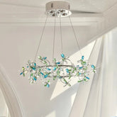 Close-up of a chrome ring chandelier adorned with clear and blue/green crystal flowers, suspended by thin wires against a white ceiling.