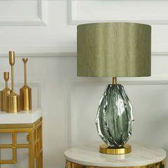 Decorative lamp with green glass base and gold accents on a marble surface.