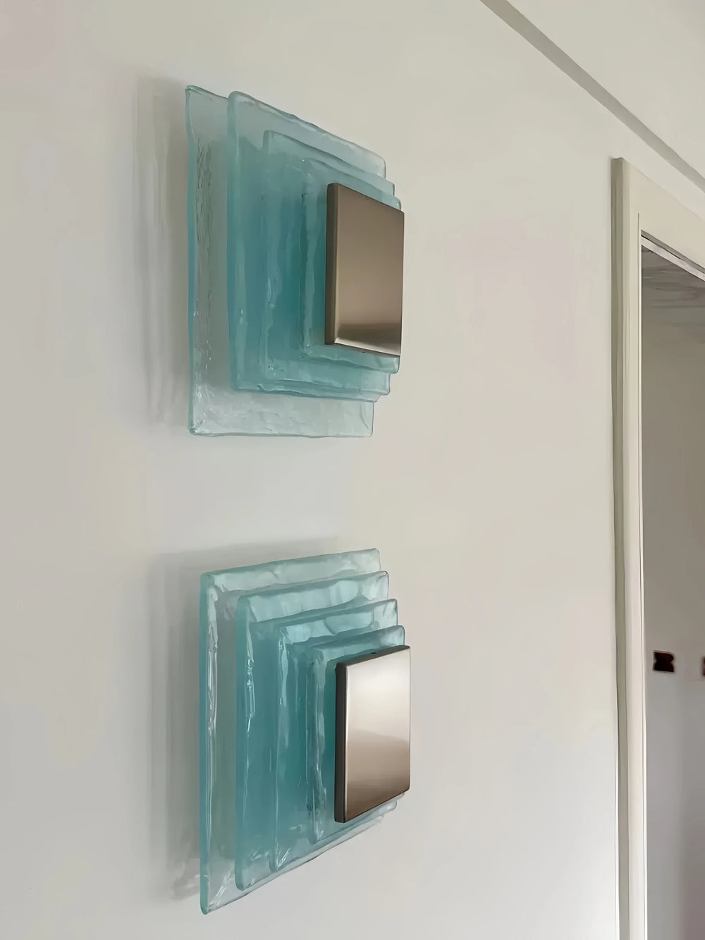 Two square wall mirrors with a teal glass frame on a white wall.