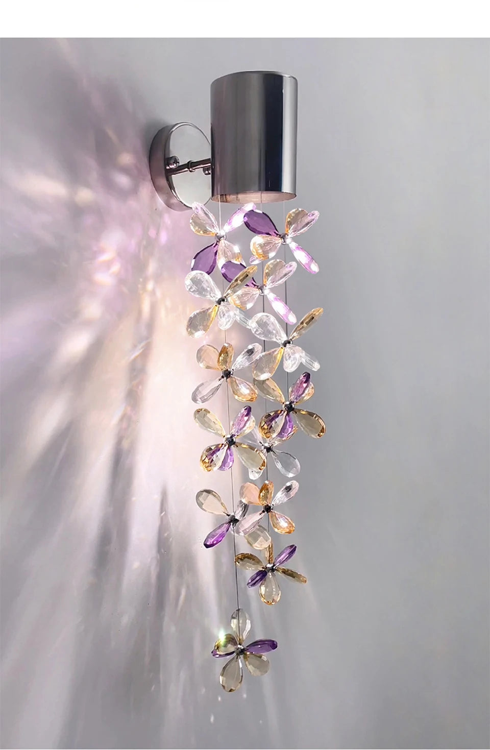 Close-up of a polished chrome wall sconce with a strand of purple and clear crystal flowers, showing the detail of the crystals.