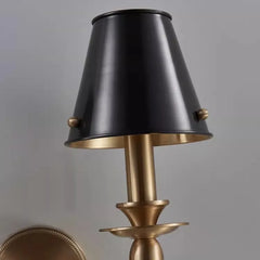Wall-mounted lamp with black shade and gold base on a gray background