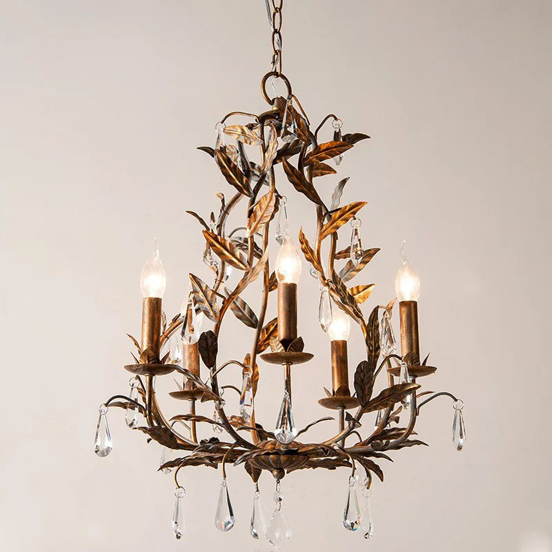 Gold wrought iron leaf chandelier with clear teardrop crystals hanging from candle-style lights, against a white background.