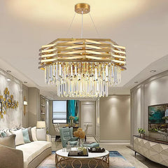 A spacious living room featuring a gold tiered crystal chandelier above a circular coffee table and a sectional sofa.