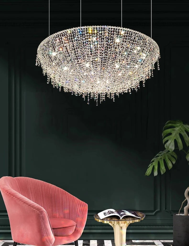 Chandelier hanging above a pink chair and small table in a room with a dark wall and green plant.