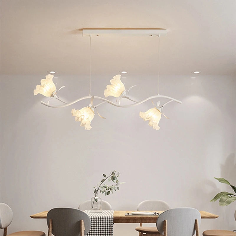 A white linear chandelier with flower-shaped shades, suspended above a dining table.