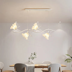 A white linear chandelier with flower-shaped shades, suspended above a dining table.